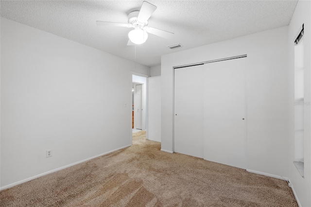 unfurnished bedroom with a textured ceiling, light colored carpet, a closet, and ceiling fan