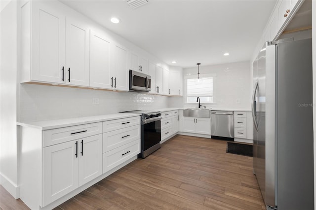 kitchen featuring stainless steel appliances, dark wood-type flooring, sink, white cabinetry, and hanging light fixtures