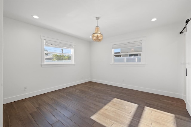 spare room featuring a barn door, dark hardwood / wood-style flooring, and a notable chandelier