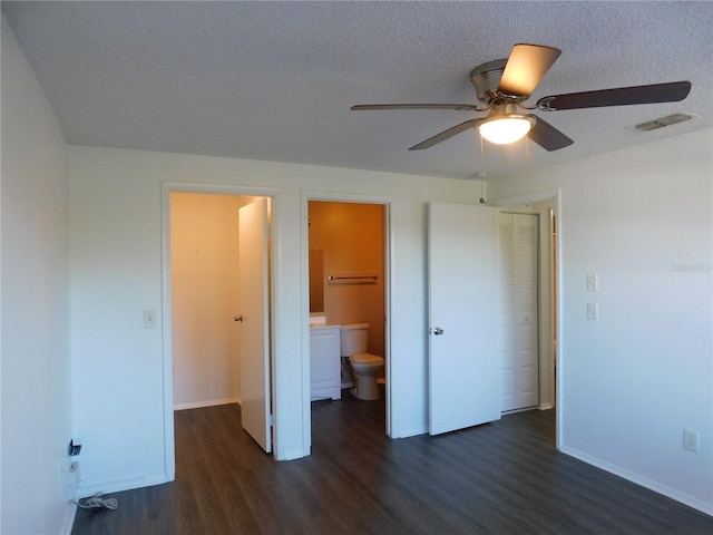 unfurnished bedroom with ensuite bath, a textured ceiling, ceiling fan, dark wood-type flooring, and a closet