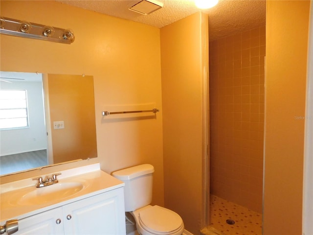 bathroom with vanity, toilet, a tile shower, and a textured ceiling