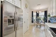 kitchen featuring stainless steel refrigerator with ice dispenser, light tile patterned floors, a notable chandelier, white cabinets, and hanging light fixtures