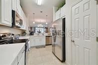 kitchen with kitchen peninsula, light tile patterned flooring, white cabinetry, and stainless steel appliances