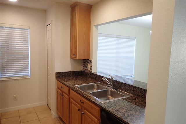 kitchen with dishwasher, light tile patterned flooring, dark stone countertops, and sink