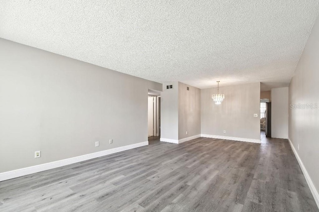 unfurnished room with hardwood / wood-style floors, a textured ceiling, and a notable chandelier