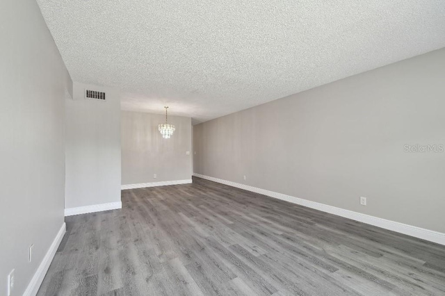 unfurnished room with wood-type flooring, a textured ceiling, and an inviting chandelier