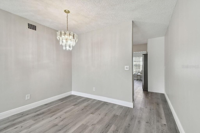 unfurnished room featuring a notable chandelier, wood-type flooring, and a textured ceiling