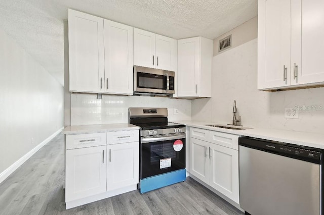 kitchen featuring light wood-type flooring, a textured ceiling, stainless steel appliances, sink, and white cabinetry