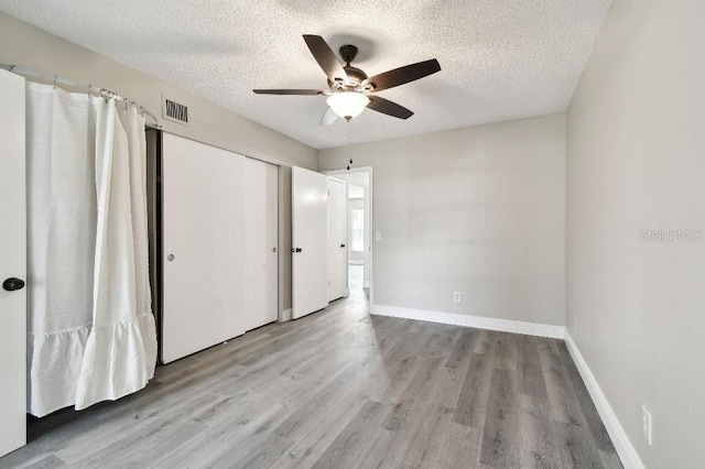 unfurnished bedroom with light wood-type flooring, a textured ceiling, a closet, and ceiling fan