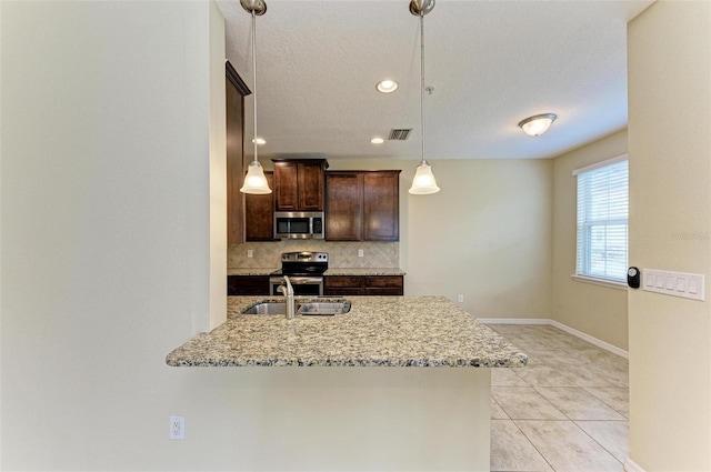 kitchen with light stone countertops, kitchen peninsula, pendant lighting, decorative backsplash, and appliances with stainless steel finishes