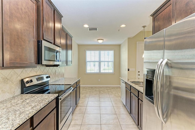 kitchen with decorative backsplash, stainless steel appliances, light stone counters, and hanging light fixtures