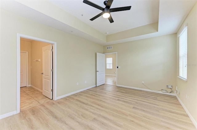 unfurnished bedroom featuring ceiling fan, a tray ceiling, and light hardwood / wood-style flooring