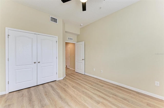 unfurnished bedroom featuring ceiling fan, light hardwood / wood-style floors, a towering ceiling, and a closet