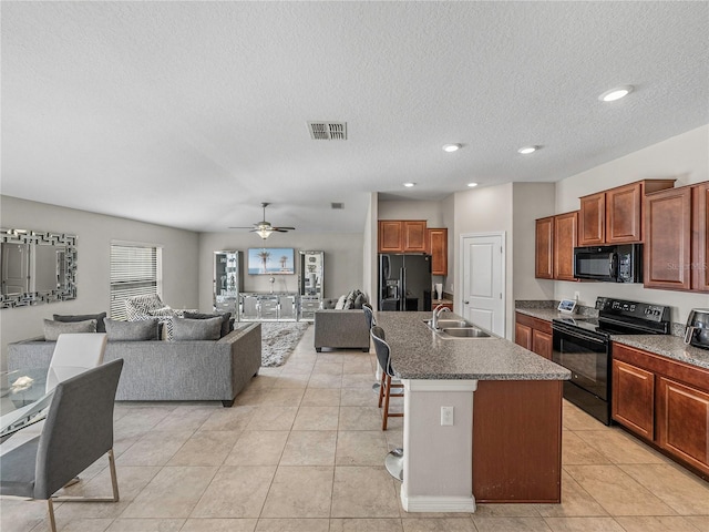 kitchen with sink, black appliances, light tile patterned floors, a breakfast bar area, and an island with sink