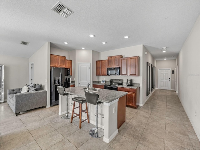 kitchen featuring a kitchen breakfast bar, a textured ceiling, sink, black appliances, and a center island with sink