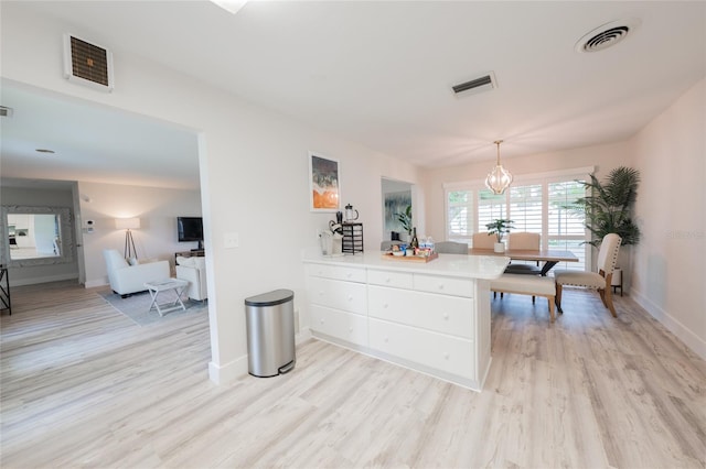 kitchen with white cabinetry, an inviting chandelier, hanging light fixtures, and light wood-type flooring