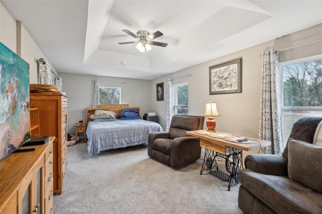 carpeted bedroom featuring a tray ceiling, multiple windows, and ceiling fan