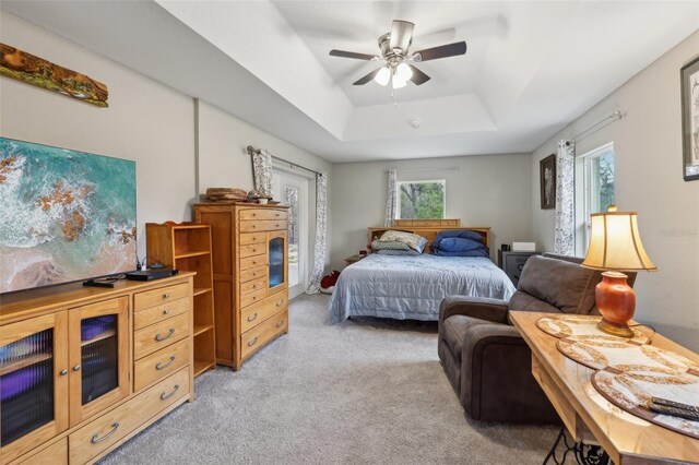 bedroom featuring multiple windows, a tray ceiling, light colored carpet, and ceiling fan