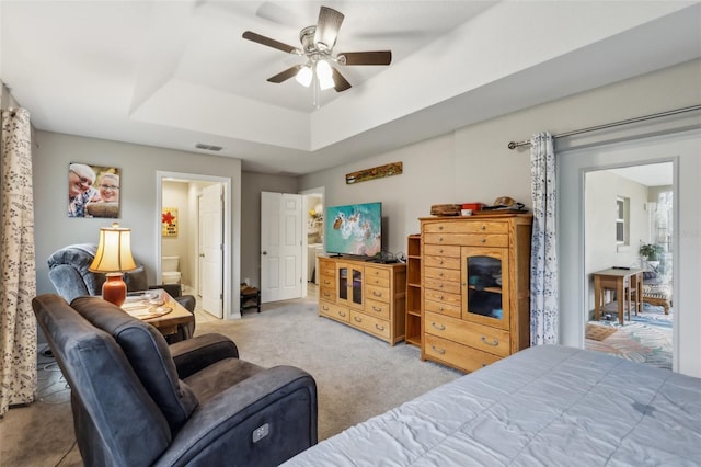 carpeted bedroom featuring a tray ceiling, ceiling fan, and ensuite bath