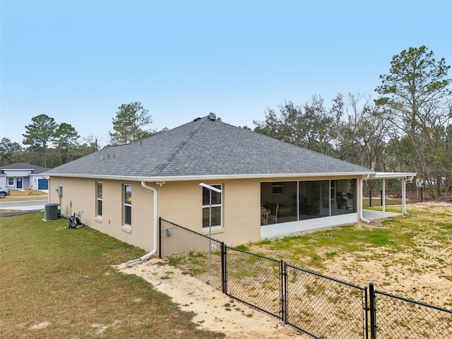 rear view of property with central air condition unit, a sunroom, and a yard