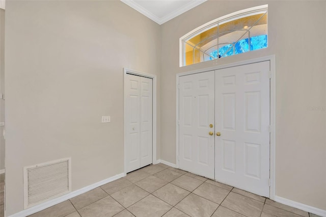 entryway with crown molding, light tile patterned floors, and a high ceiling