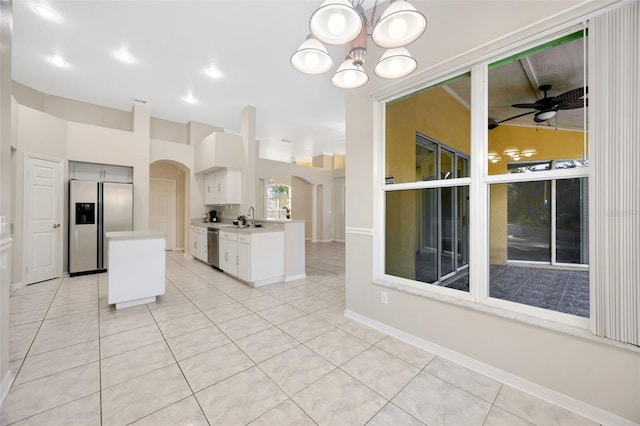 kitchen with ceiling fan with notable chandelier, stainless steel appliances, sink, light tile patterned floors, and white cabinets