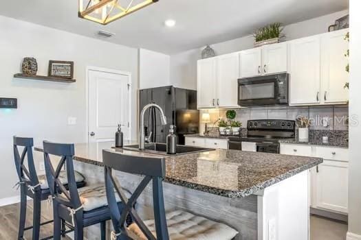 kitchen with a kitchen breakfast bar, tasteful backsplash, black appliances, a center island with sink, and white cabinetry