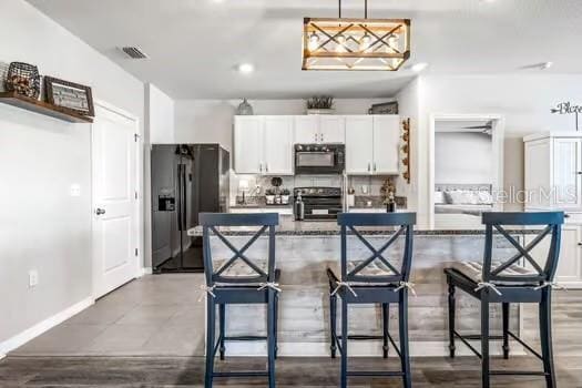 kitchen with a kitchen breakfast bar, white cabinetry, hanging light fixtures, and black appliances