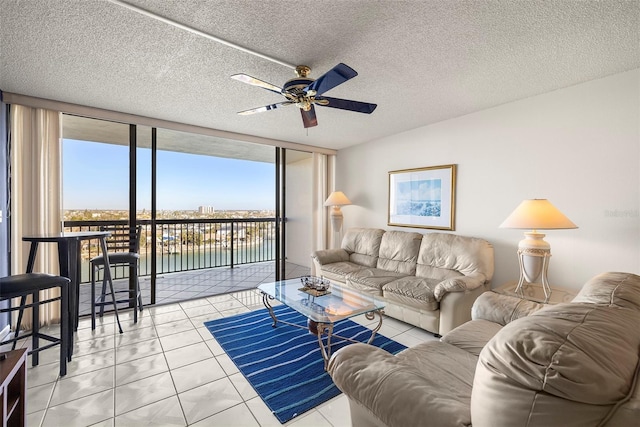 tiled living room featuring ceiling fan, a water view, a wall of windows, and a textured ceiling