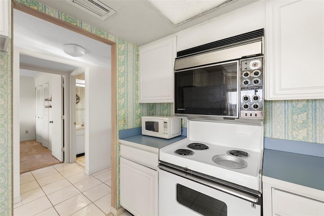 kitchen with a textured ceiling, white cabinets, light tile patterned flooring, and white appliances