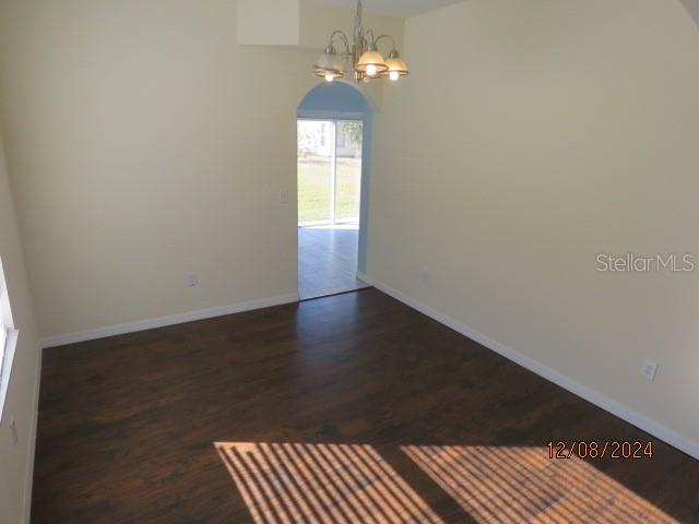 empty room with a chandelier and dark wood-type flooring