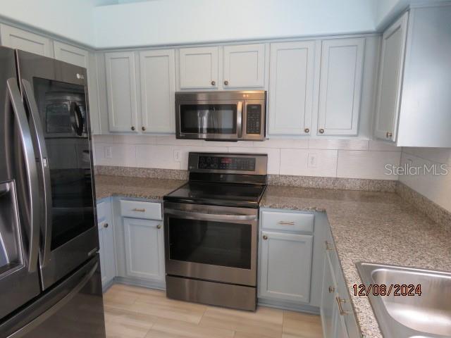 kitchen featuring light stone countertops, sink, light hardwood / wood-style floors, decorative backsplash, and appliances with stainless steel finishes