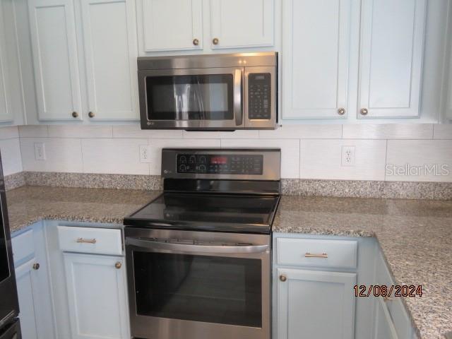 kitchen with decorative backsplash, white cabinets, stainless steel appliances, and light stone counters