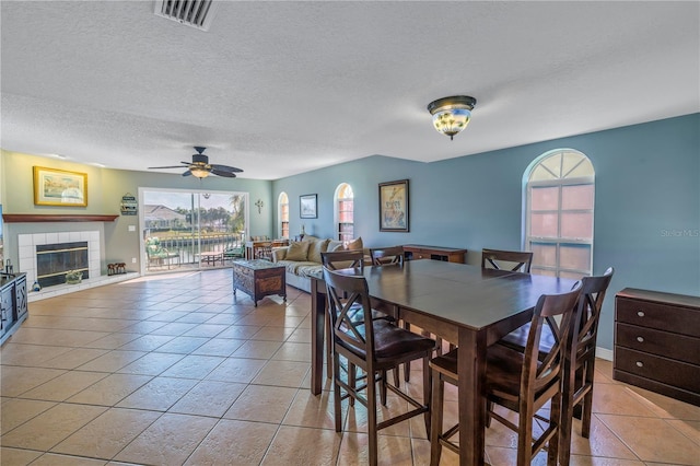 tiled dining room with ceiling fan, a textured ceiling, and a tile fireplace