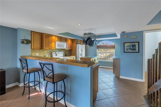 kitchen featuring a kitchen bar, kitchen peninsula, decorative backsplash, and white appliances