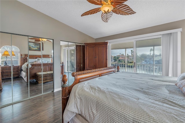 bedroom with a textured ceiling, two closets, ceiling fan, dark hardwood / wood-style floors, and lofted ceiling