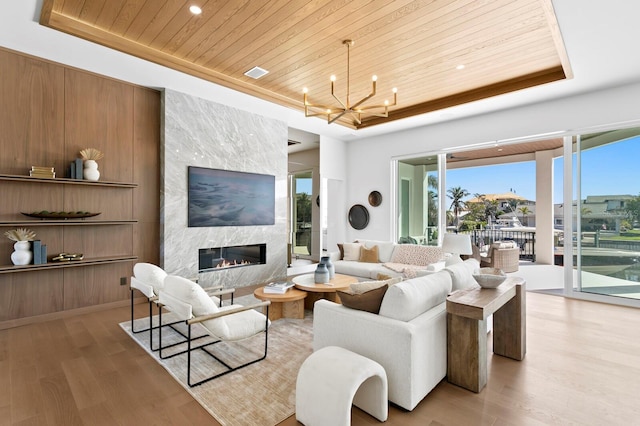 living room with a notable chandelier, a tray ceiling, a fireplace, wooden ceiling, and light wood-type flooring