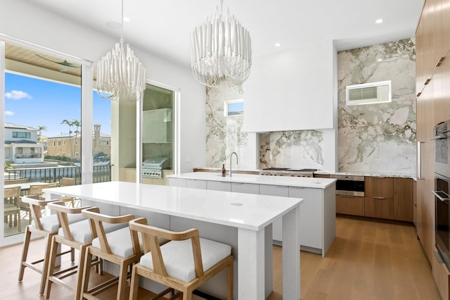 kitchen featuring an inviting chandelier, decorative light fixtures, a kitchen island with sink, and tasteful backsplash