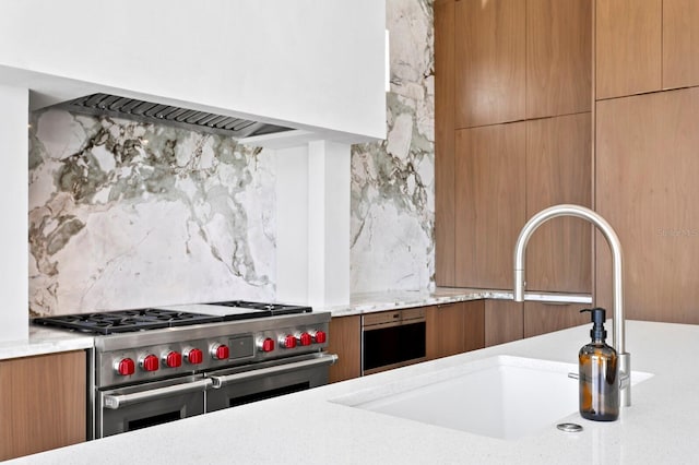 kitchen with sink, premium range hood, tasteful backsplash, light stone counters, and range with two ovens