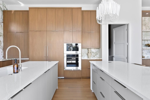 kitchen featuring white cabinetry, double oven, a notable chandelier, light stone countertops, and decorative light fixtures