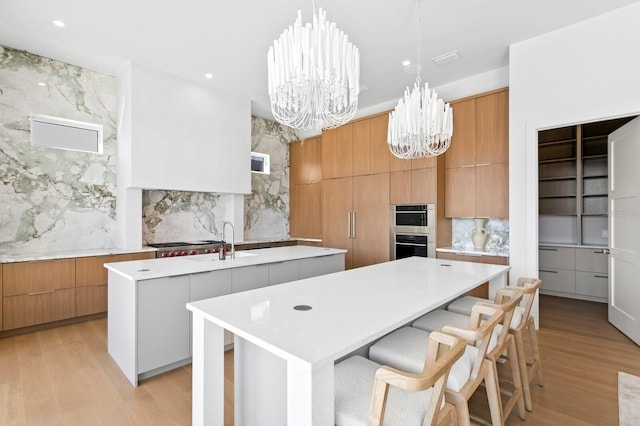 kitchen featuring an inviting chandelier, hanging light fixtures, a large island with sink, and light wood-type flooring