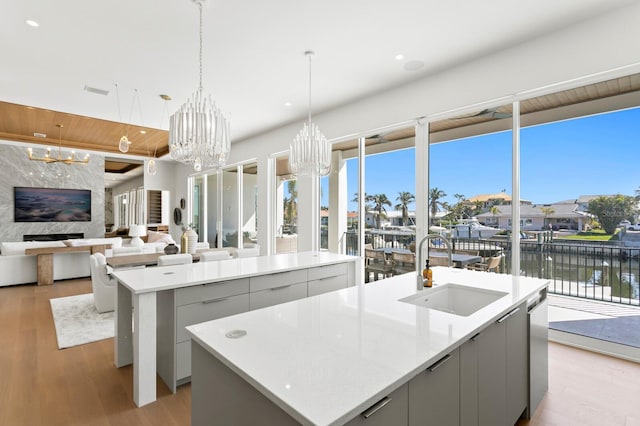 kitchen with an island with sink, sink, gray cabinetry, and a notable chandelier