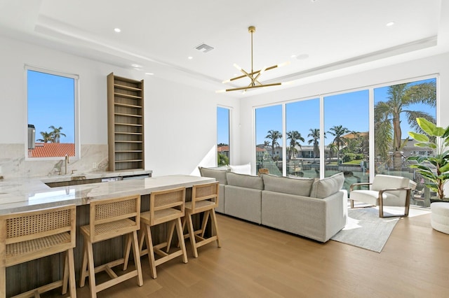 living room with sink, light hardwood / wood-style flooring, a chandelier, and a tray ceiling