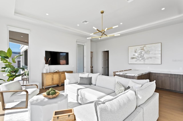 living room featuring an inviting chandelier, a raised ceiling, and light wood-type flooring