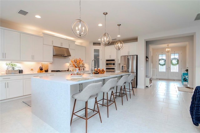 kitchen with visible vents, under cabinet range hood, a breakfast bar, decorative backsplash, and stainless steel appliances