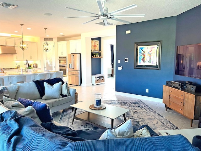 living area featuring light tile patterned floors, a ceiling fan, visible vents, baseboards, and a textured ceiling