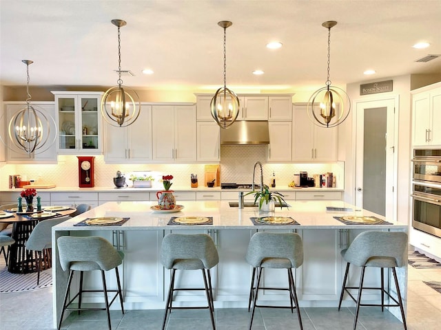 kitchen with tasteful backsplash, visible vents, under cabinet range hood, decorative light fixtures, and white cabinets