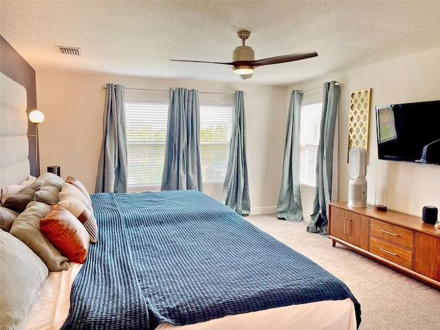 bedroom with visible vents, baseboards, light colored carpet, a textured ceiling, and a ceiling fan