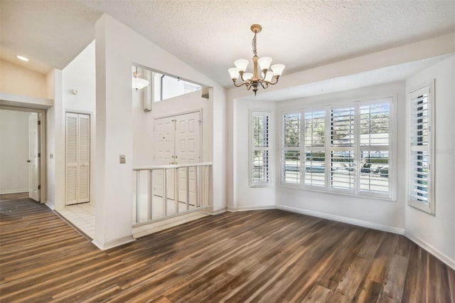 unfurnished dining area with a chandelier, a textured ceiling, dark hardwood / wood-style floors, and vaulted ceiling