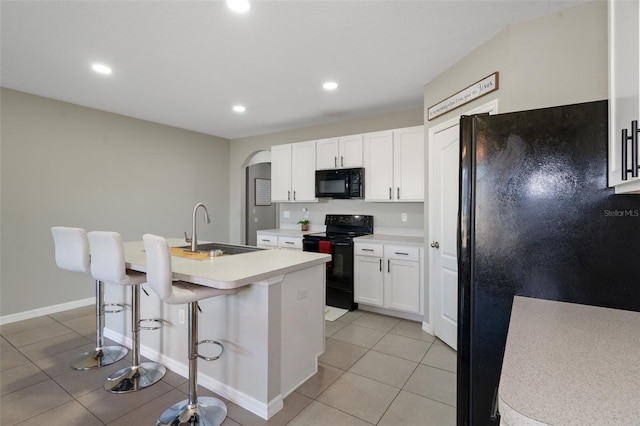 kitchen featuring a breakfast bar, sink, black appliances, white cabinetry, and an island with sink